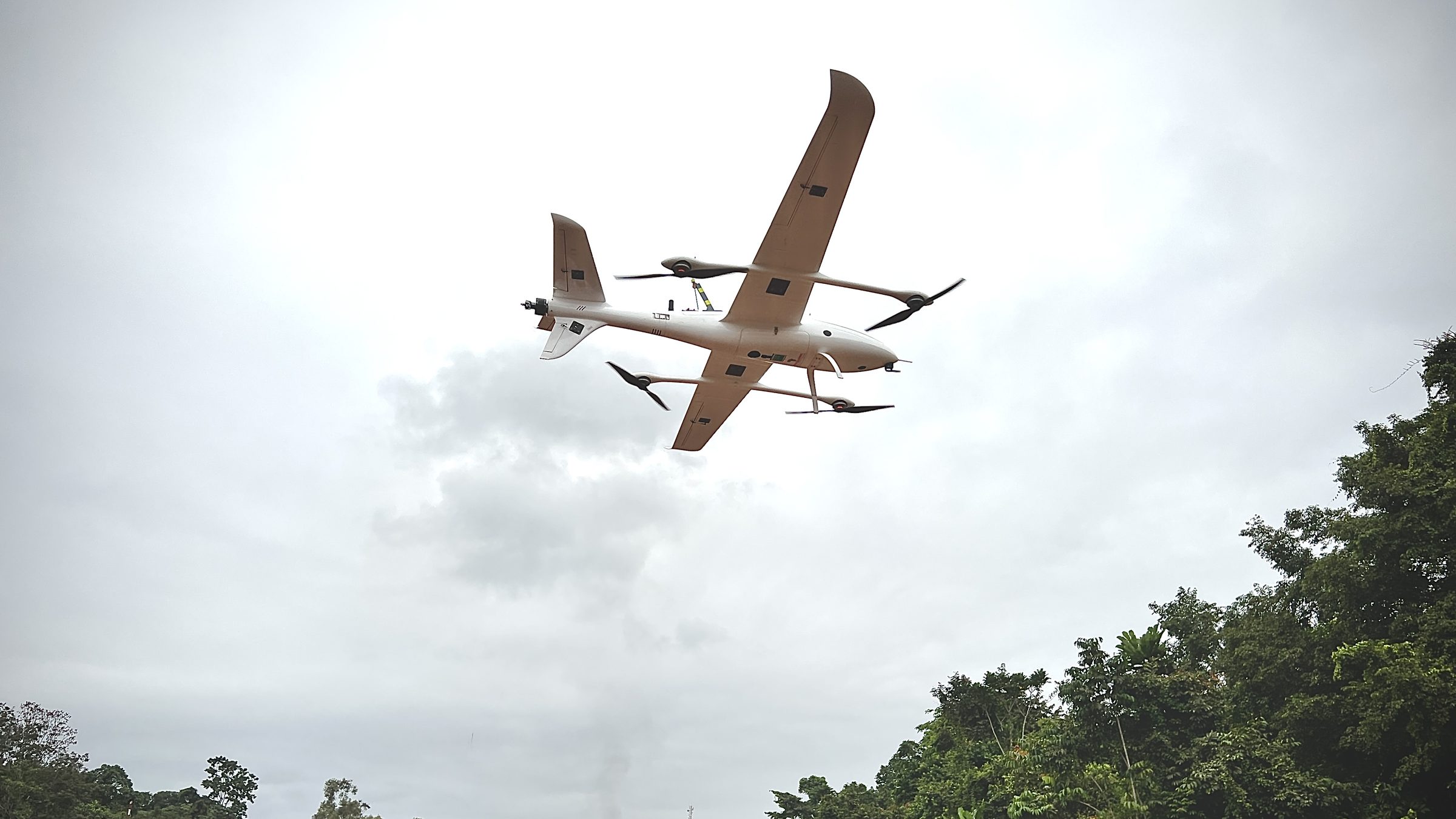 A Pilotless fixed-wing VTOL aircraft climbing out over a red dirt road
